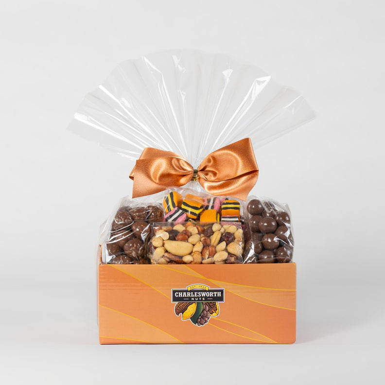 A festive gift basket adorned with a vibrant orange ribbon. The basket is brimming with a delightful assortment of treats including Beer Nuts, Chocolate Peanuts, Spicy Crackers, and more delicious snacks