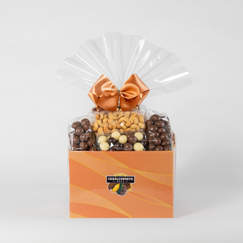 Adorned with a vibrant orange ribbon, this delightful gift basket overflows with an assortment of treats including beer nuts, chocolate bullets, salted cashews, crackers, and more. 