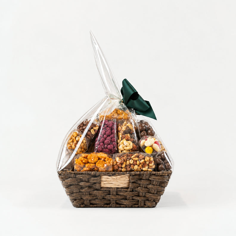 A gourmet snack and candy gift basket in a brown woven basket, wrapped in clear cellophane with a dark green bow.