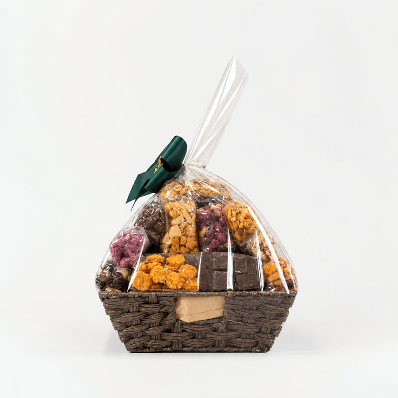 A wicker gift basket filled with assorted packaged snacks and nuts, wrapped in clear cellophane and tied with a dark green ribbon.