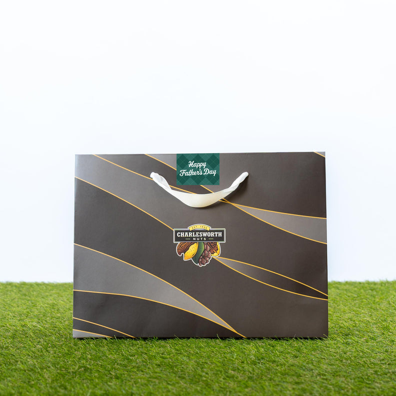 Charlesworth Nuts The Man Bag — a dark gift bag with gold wave design, Charlesworth Nuts logo, and Happy Father's Day tag.