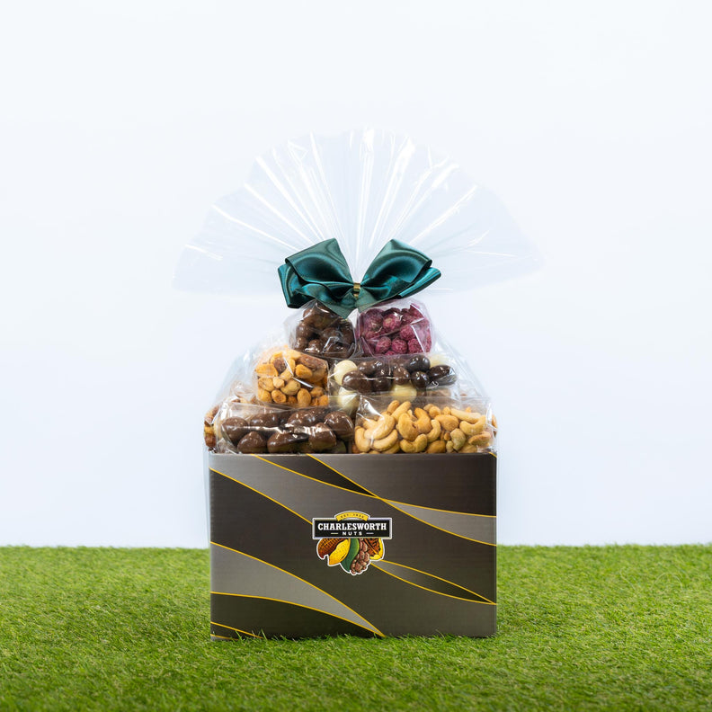 A Father's Day gift basket of assorted snacks and nuts in a black branded box, wrapped in clear cellophane and tied with a green green bow.